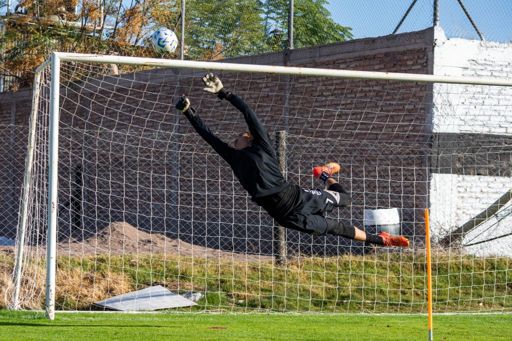 Goalkeeper making a diving save as the ball crosses the goal line, illustrating a goal event relevant to Over/Under goals betting